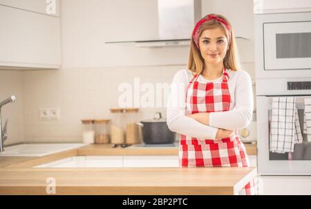 Junge Frau steht selbstbewusst in der Küche mit Schürze. Stockfoto