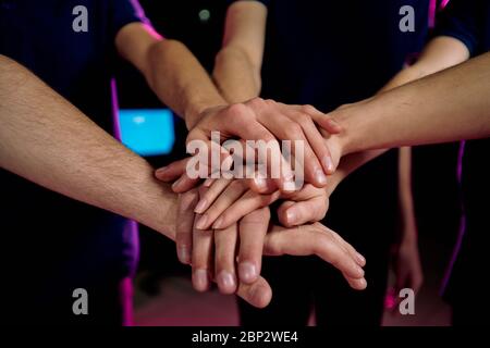 Handhaufen junger zeitgenössischer erfolgreicher Cybersport-Videospieler, die durch ihre Geste Kameradschaft und Zusammengehörigkeit ausdrücken Stockfoto