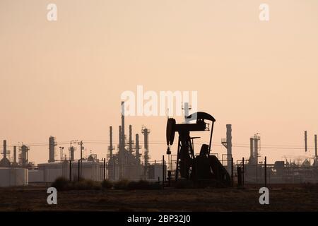 Pumpjack mit einer Ölraffinerie im Hintergrund und verschwommenem Himmel Stockfoto