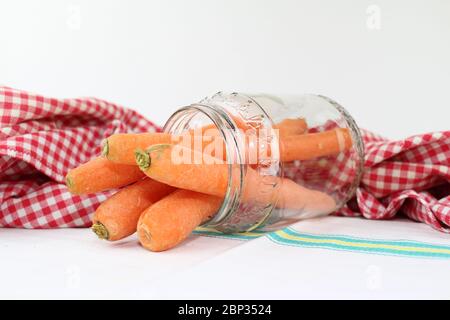 Karotten im Glasgefäß, mit der rot-weiß karierten Tischdecke und einem Baumwolltuch mit farblich bedruckter Linie. Stockfoto