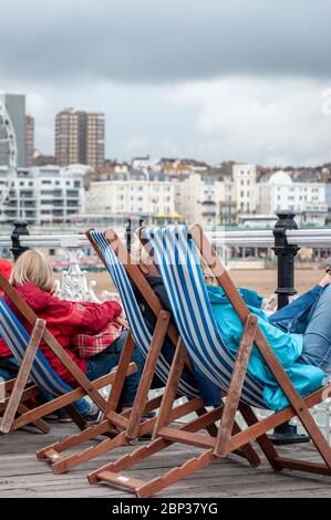 Menschen, die an einem trüben Sommertag in Brighton, Großbritannien, in Liegestühlen am Brighton Pier sitzen Stockfoto