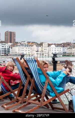 An einem langweiligen Sommertag in Brighton, Großbritannien, sitzen Leute auf Liegestühlen am Brighton Pier Stockfoto