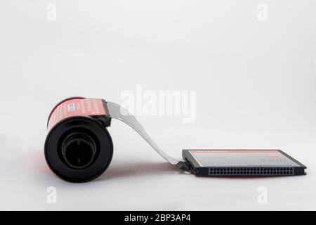 35-mm-Film, der aus der Kassette auf eine 16-GB-Speicherkarte rollt, als ob die beiden angeschlossen wären, vor einem weißen Hintergrund mit Platz für Text Stockfoto