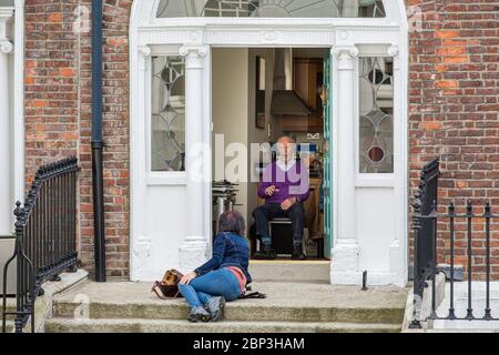 Besuch älterer Verwandter oder Freunde in Dublin während der Covid-19 Pandemie. Der alte Mann spricht von seiner Tür zur Frau, die auf seinen Stufen sitzt. Sicherheitsabstand Stockfoto