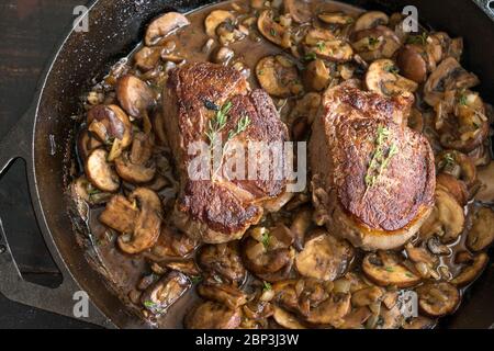 Filet Mignon in Pilzweinsauce: Zwei Filet Mignon Steaks mit einer cremigen Pilzsauce in einer gusseisernen Pfanne garniert mit frischen Thymian-Zweige Stockfoto