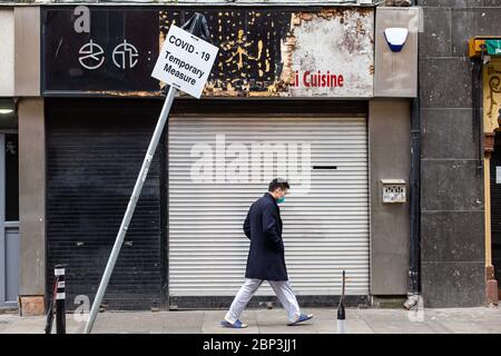 Asian Mann trägt Schutzmaske vorbei geschlossen Shop und schiefen Zeichen - Covid-19 vorübergehende Maßnahme. Wirtschaftliche Auswirkungen des Coronavirus Irland. Stockfoto