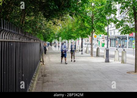 Fußgänger, die in Dublin mit Gesichtsmasken spazieren und die soziale Distanzierungsregel einhalten, indem sie im Freien in öffentlichen Bereichen Sicherheitsabstand einhalten. Stockfoto