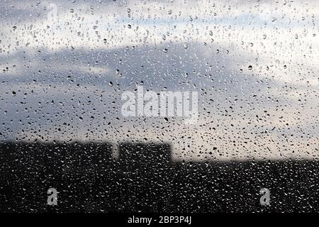 Regentropfen auf dem Fensterglas auf verschwommenem Hintergrund des bewölkten Himmels. Schöne Wassertropfen, regnerisches Wetter in der Stadt Stockfoto