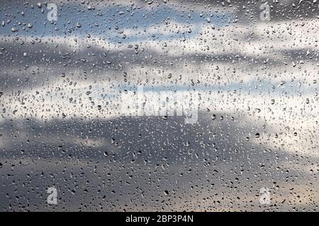 Regentropfen auf dem Fensterglas auf verschwommenem Hintergrund des bewölkten Himmels. Schöne Wassertropfen, regnerisches Wetter in der Stadt Stockfoto