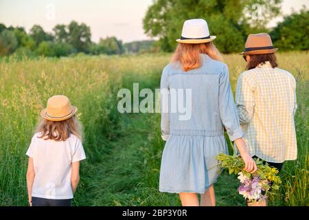 Mutter und Kinder zwei Töchter, die auf einer Landstraße durch die Wiese laufen Stockfoto