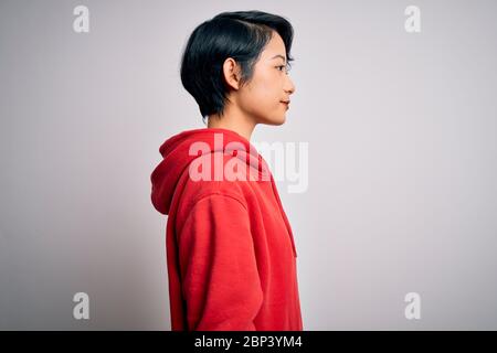 Junge schöne asiatische Mädchen tragen lässige Sweatshirt mit Hoodie über weißem Hintergrund auf der Seite suchen, entspannen Profil Pose mit natürlichen Gesicht mit conf Stockfoto