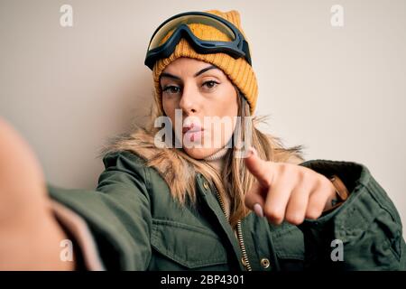 Junge Brünette Skifahrer Frau in Schneekleider und Skibrille machen Selfie mit Kamera zeigt mit dem Finger auf die Kamera und zu Ihnen, Handzeichen, Positi Stockfoto