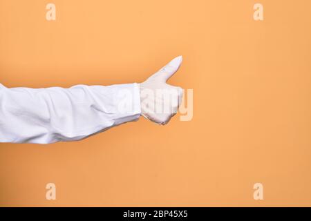 Hand einer Person, die medizinischen chirurgischen Handschuh tun ok Zeichen mit Daumen nach oben über isolierten gelben Hintergrund Stockfoto