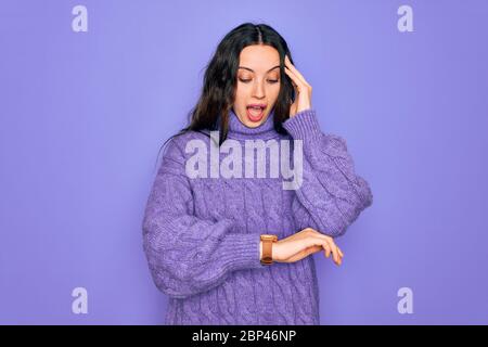 Junge schöne Frau mit lässigen Rollkragen Pullover über lila Hintergrund stehend Blick auf die Uhr Zeit besorgt, Angst vor dem Erhalten spät Stockfoto