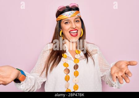 Junge hispanische Hippie Frau, die Mode Boho Stil und Sonnenbrille über rosa Hintergrund lächelnd fröhlich mit Händen geben Hilfe und accep Stockfoto