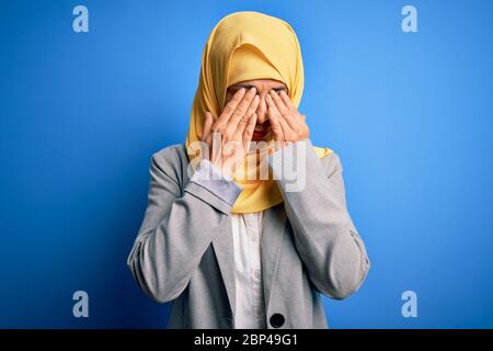 Mittelalter Brünette Geschäftsfrau trägt muslimischen traditionellen Hijab über blauem Hintergrund reiben Augen für Müdigkeit und Kopfschmerzen, schläfrig und müde expre Stockfoto