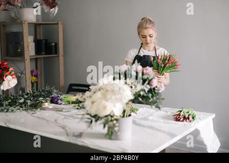 Professionelle junge Frau Floristin tragen Schürze Herstellung Blumenarrangement aus frischen Tulpe am Tisch Stockfoto