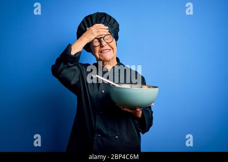 Senior schöne grau-haarige Köchin Frau trägt Kocher Uniform und Hut mit Schneebesen und Schüssel mit Hand auf Kopf gestresst, schockiert vor Scham und Surpris Stockfoto