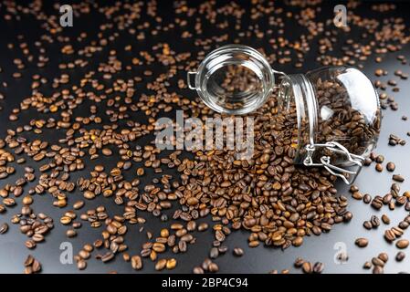 Frische, geröstete Kaffeebohnen in einem offenen, umgedrehten Glas auf einem schwarzen Tisch mit Kaffeebohnen gefüllt. Stockfoto