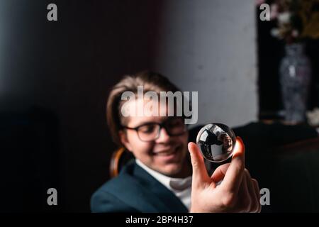 Junger Mann, der eine durchsichtige Glaskugel in der Hand hält Stockfoto