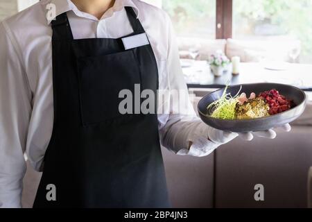 Kellner hält einen Teller mit Teer-Teer mit getrockneten Cranberries und Daikon in einem Restaurant Stockfoto