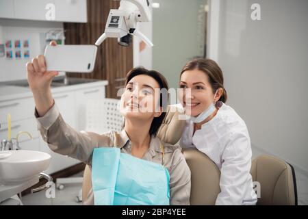 Arzt und Patient Selfie im Operationssaal. Glücklicher Patient hält EIN Smartphone Stockfoto