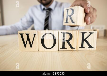 Es schreibt das Wort Arbeit auf Holzblöcke. Der Mann im Anzug legt den Block auf die Oberseite. Stockfoto