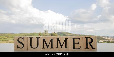 Sommertext auf Holzblöcken. Ein Foto wurde auf dem Tisch gemacht. Im Hintergrund sind Himmel und Berge. Stockfoto