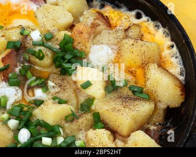 Spiegeleier mit Kartoffeln und grünen Zwiebeln in einer Pfanne Stockfoto