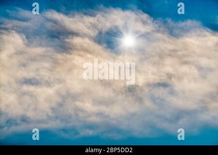 Ein strahlender Stern scheint durch die weißen Wolken am blauen Himmel Stockfoto