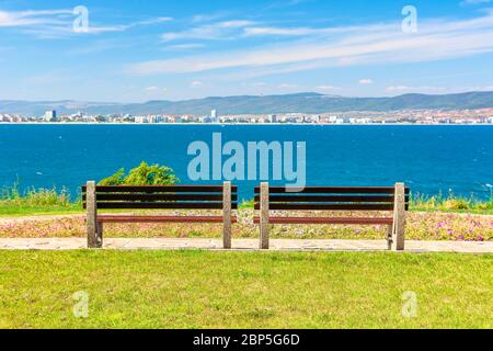 Zwei Bänke am sonnigen Strand. Schöne Skyline Blick aus leeren Park mit gepflasterten Fußweg am Meer. Stadt und Berg in der Ferne ben Stockfoto