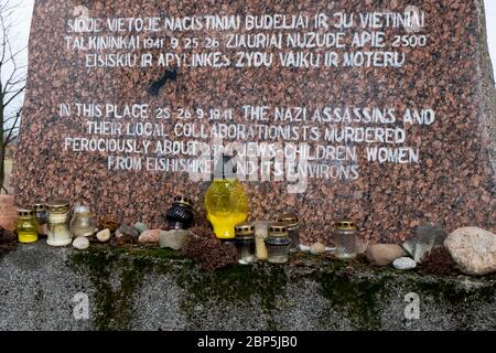 Kerzen und Steine auf dem braunen Granitmarker, der an den Ort erinnert, an dem alle jüdischen Frauen und Kinder aus der Stadt hingerichtet wurden. In Eišiš Stockfoto