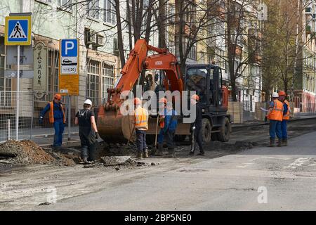 Perm, Russland - 05. Mai 2020: Arbeiter versammelten sich um einen Bagger diskutieren über die Arbeit an der bevorstehenden Grabungen auf einer Stadtstraße Stockfoto