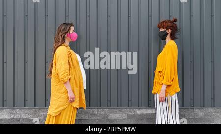 Zwei Frauen in Schutzmasken und gelber Kleidung stehen in der Ferne. Das Konzept der sozialen Distanz. Schwarzer Hintergrund Stockfoto