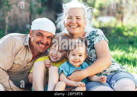 Glückliche Familie lächelnd Großvater Großmutter mit Enkelkindern sitzen auf Freiluft-Rasen an einem sonnigen Tag Stockfoto