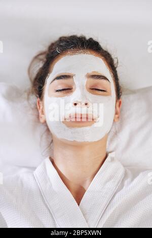 Lächelnde junge Frau ruht in schlecht mit entgiftenden und aufhellenden weißen Ton Maske Stockfoto