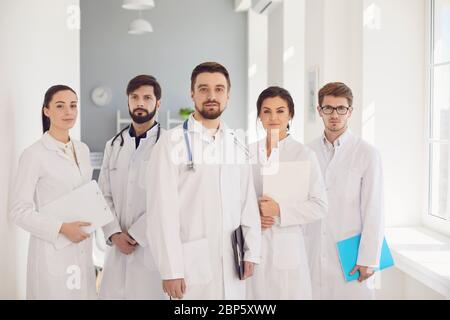 Eine Gruppe von selbstbewussten Praktizierenden Ärzten in weißen Mänteln lächelt vor dem Hintergrund der Klinik. Stockfoto