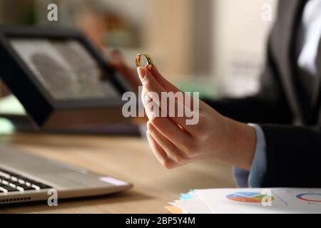 Nahaufnahme der Managerin Hände halten Ehering nach der Scheidung sitzen auf einem Schreibtisch im Homeoffice in der Nacht Stockfoto