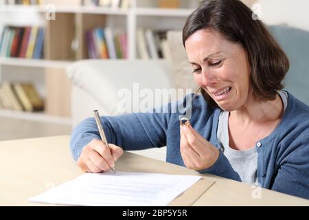 Traurige Frau weinend Unterzeichnung Scheidung Papiere Blick auf Ehering im Wohnzimmer zu Hause Stockfoto