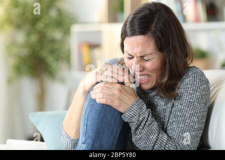 Erwachsene Frau mit Schmerzen und Knieschmerzen sitzt auf einer Couch zu Hause Stockfoto