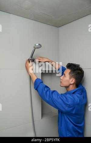 Ernst vietnamesischen Klempner in Uniform Fixierung undicht Duschkopf im Bad Stockfoto