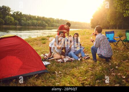 Junge Leute machen Seifenblasen, während sie auf dem Gras in der Natur sitzen. Stockfoto