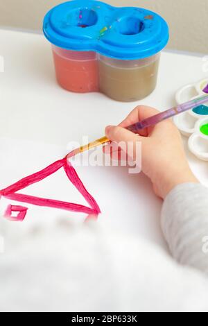 Nahaufnahme der Hand des Kindes, das ein Hausdach auf weißem Papier zeichnet. Konzept des kreativen Lernens. Stockfoto