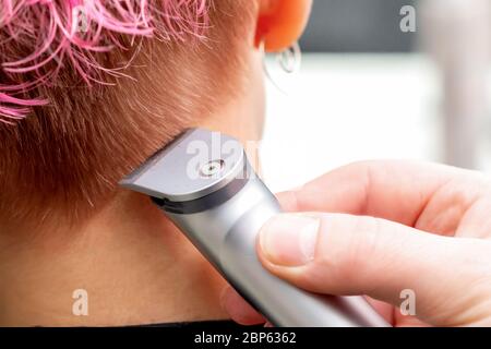 Rückansicht Friseur Hand ist Rasieren rosa Haar der Frau mit elektrischen Trimmer im Friseursalon, Nahaufnahme. Stockfoto