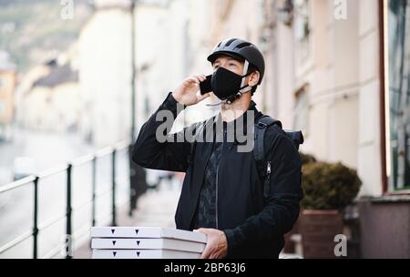 Lieferung Mann Kurier mit Gesichtsmaske und Smartphone liefert Pizza in der Stadt. Stockfoto