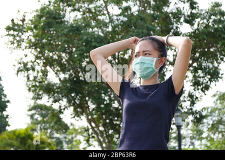 Junge asiatische Frau in medizinischen Schutzmaske tun Stretching Warmup vor der Übung am Morgen.Workout im Freien. Konzept der gesunden Stockfoto