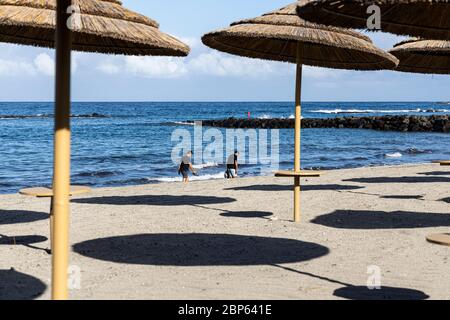 Die Menschen flüchten zwischen den unbenutzten Sonnenschirmen, die während der ersten Phase der Deeskalation des Covid 1 am Strand von Playa Fanabe Sport treiben Stockfoto