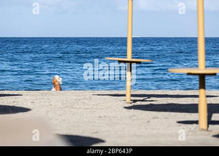 Die Menschen flüchten zwischen den unbenutzten Sonnenschirmen, die während der ersten Phase der Deeskalation des Covid 1 am Strand von Playa Fanabe Sport treiben Stockfoto