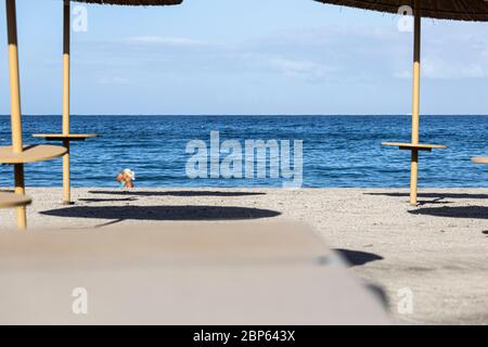 Die Menschen flüchten zwischen den unbenutzten Sonnenschirmen, die während der ersten Phase der Deeskalation des Covid 1 am Strand von Playa Fanabe Sport treiben Stockfoto