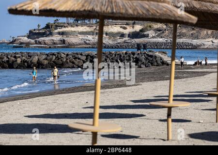 Die Menschen flüchten zwischen den unbenutzten Sonnenschirmen, die während der ersten Phase der Deeskalation des Covid 1 am Strand von Playa Fanabe Sport treiben Stockfoto